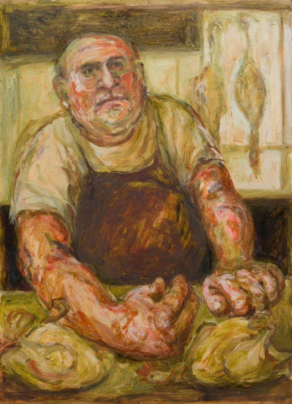 A bald butcher in an apron with big red hands and dead chicken to the front and behind.