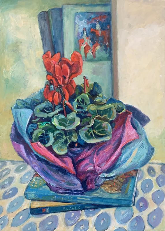 A scarlet Cyclamen wrapped in tissue sitting on 2 angel books .